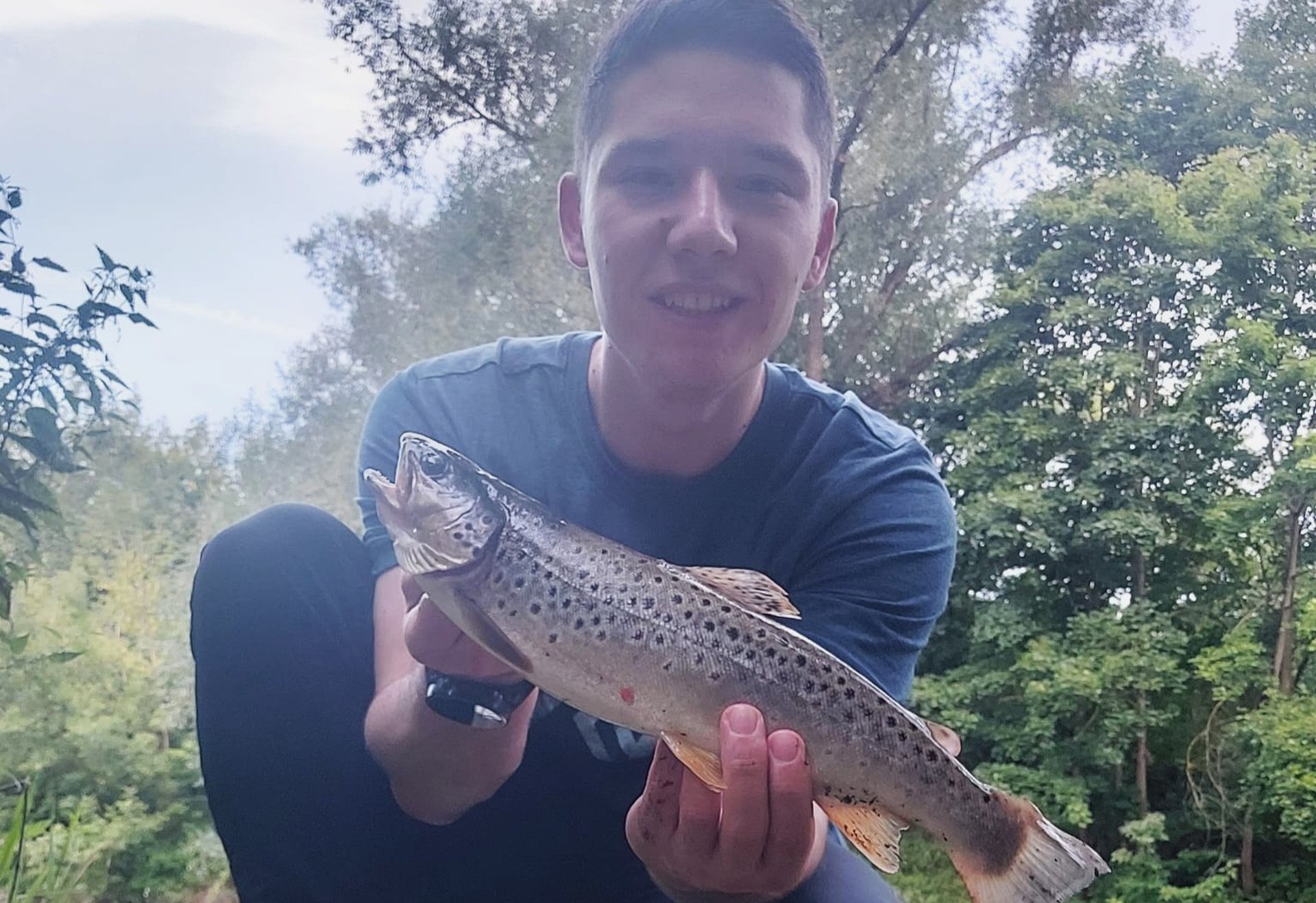 Ein junger Mann hält eine gefangene Bachforelle