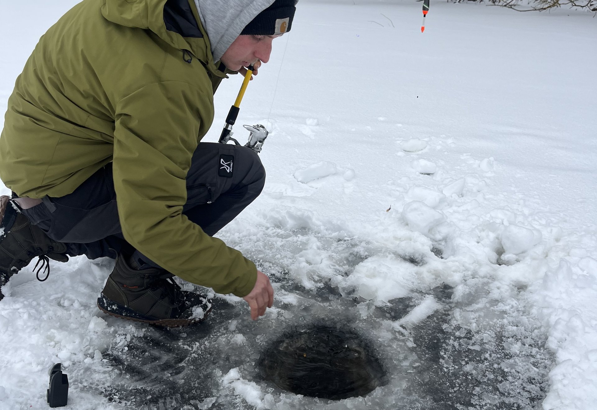Angler kniet auf zugefrorenem See und kontrolliert ein Eisloch beim Eisangeln.